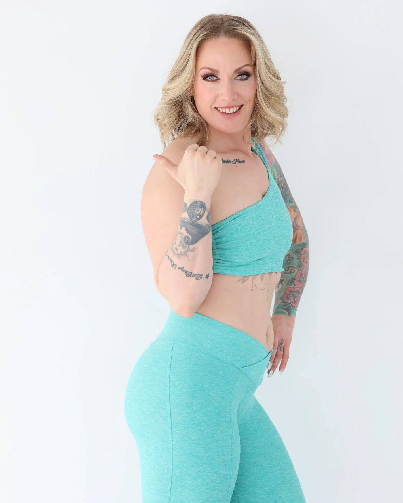 Deidra Skappak, founder of In Good Hands, smiling in teal activewear against a bright white wall