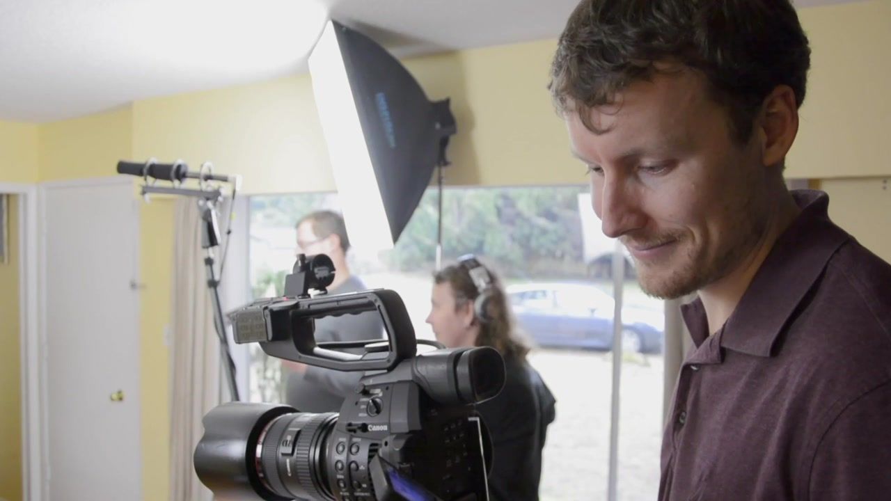 Zachary Tannar on set, checking his notes beside a cinema camera and studio lights