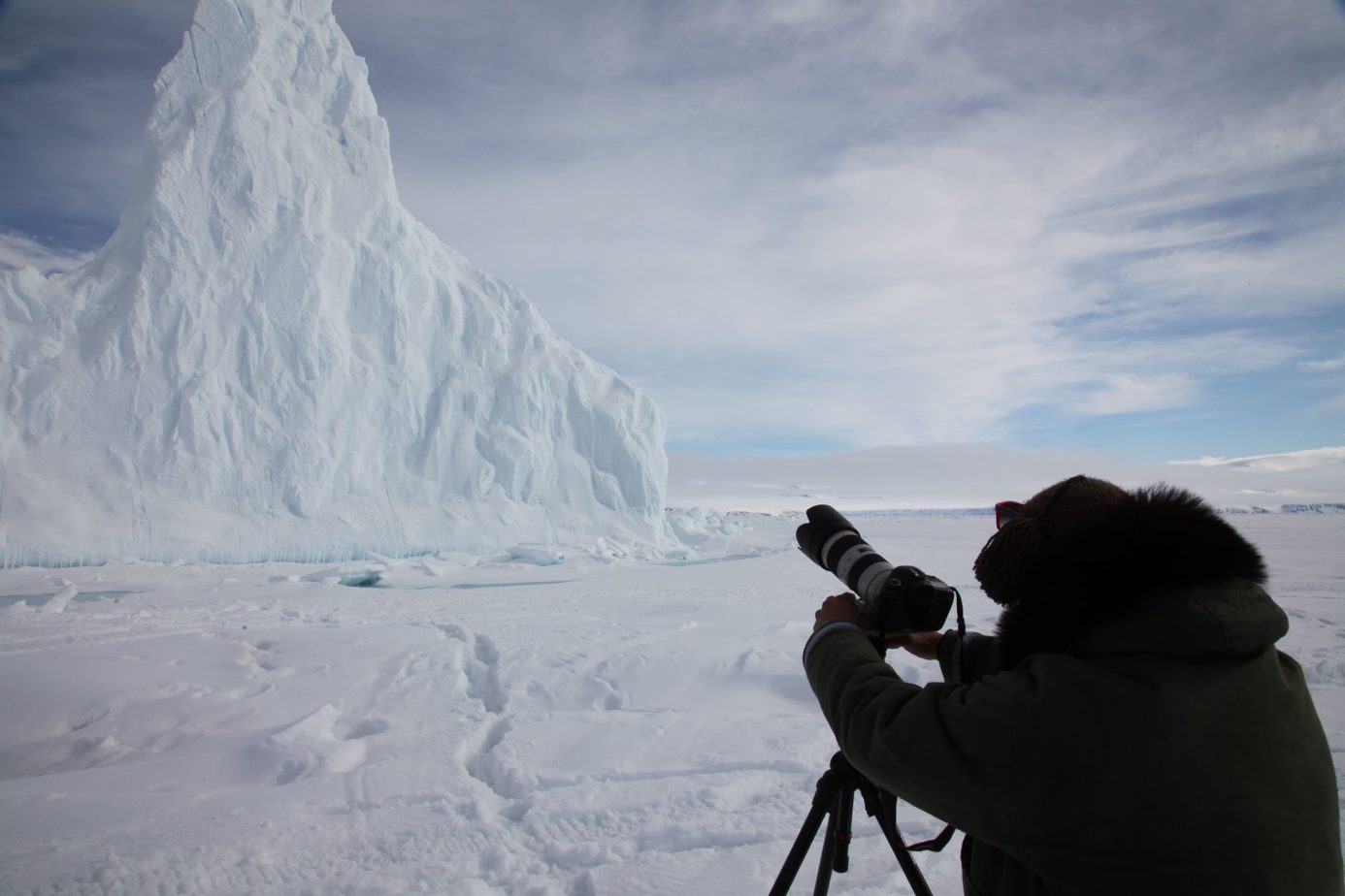 A photographer with a long lens on a tripod, beside an iceberg on the sea ice