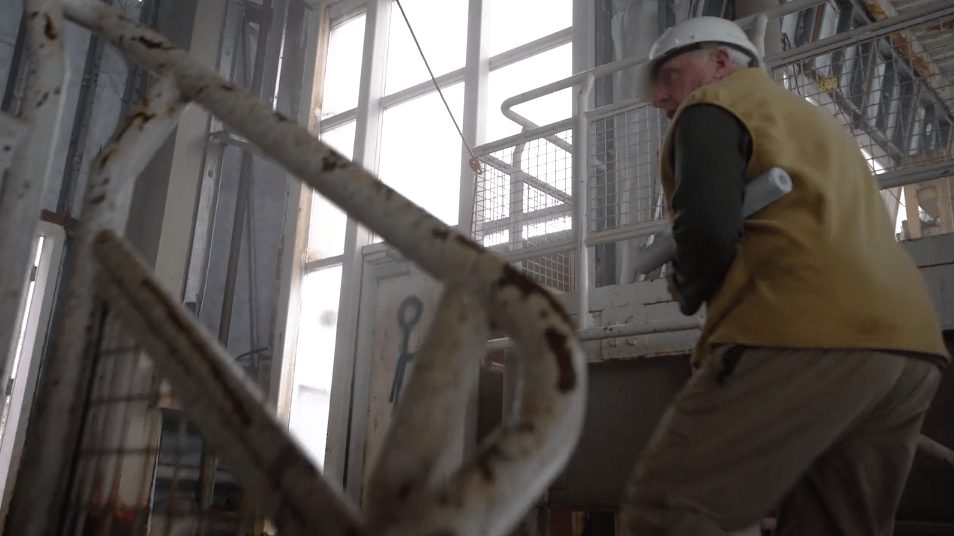 A man in a hard hat and vest climbing an old staircase inside a building, from the Bring Back McBarge video