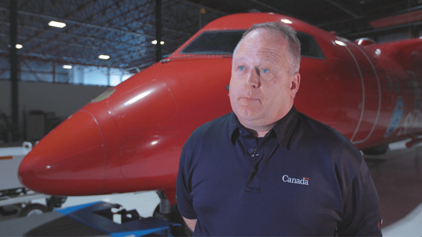 A Coast Guard crew member in front of a red and white Dash 8 plane in a hangar