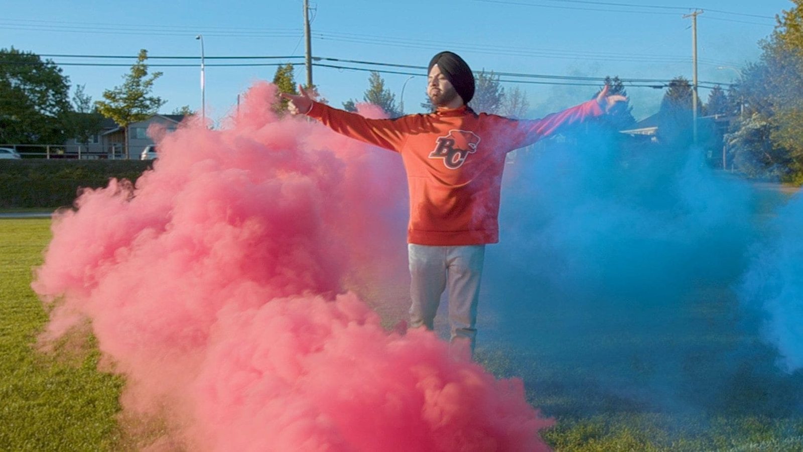 A man with arms wide in clouds of pink and blue coloured smoke