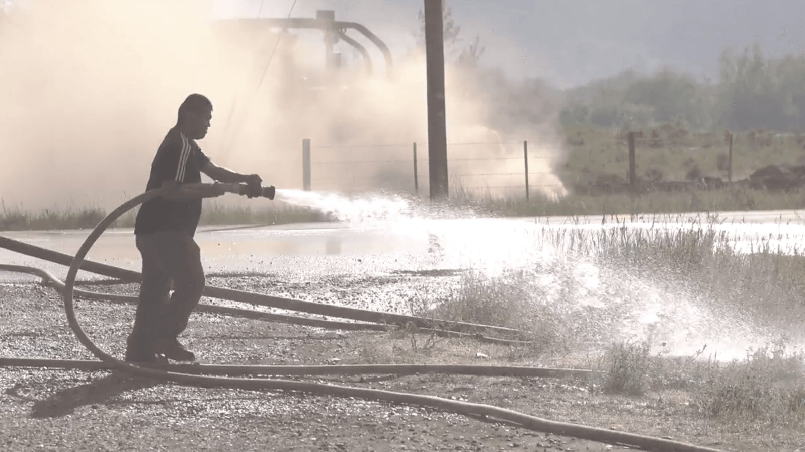A man spraying a fire hose into wildfire smoke